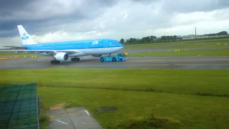 KLM-Airline-Flugzeug,-Gezogen-Von-Einem-LKW-Schlepper-Auf-Einer-Landebahn-Mit-Regnerischen-Wolken-Im-Hintergrund