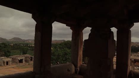 Pan-view,-viewing-through-the-temple-ruins-the-Virupaksha-temple-gopuram-from-top-of-the-HemaKuta-hill-at-Hampi