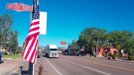 18-wheeler-driving-past-on-the-4th-of-July-in-the-city-of-Panguitch,-Utah-with-US-flag-in-the-foreground
