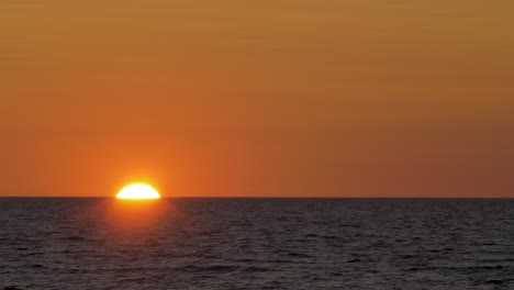 Romantic-sunset-over-the-calm-Baltic-sea,-big-red-Sun-sets-over-the-horizon-in-summer,-medium-shot-from-a-distance