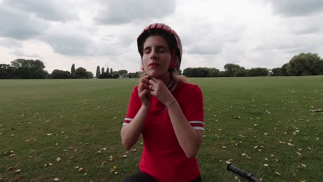 Caucasian-young-female-cyclist-puts-on-red-helmet