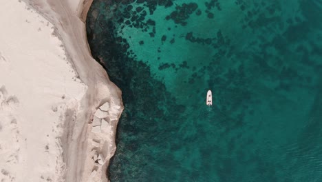 Boat-moving-next-to-a-cliff-in-shalow-clear-waters-in-patagonia-from-a-drone-top-shot-slowmotion