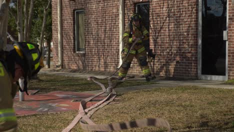 Feuerwehrleute-Ziehen-Einen-Feuerlöschschlauch-Zu-Einem-Gebäude,-Um-Sich-Auf-Die-Brandbekämpfung-Vorzubereiten