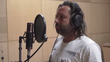 Man-with-long-hair-recording-vocals-in-studio,-side-middle-shot-view
