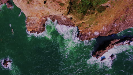 Aerial-flying-sideways-over-steep-ocean-cliffs,-breaking-waves,-rocks