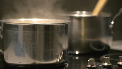 Close-up-of-two-pans-simmering-on-a-cooktop-with-steam-rising