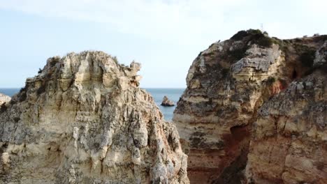 Rising-up-over-limestone-rock-formations-in-Algarve,-Portugal-to-reveal-boats-and-sea-cliffs,-Aerial