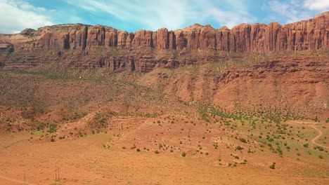 Drone-shot-of-a-steep-red-rock-cliff-towering-over-a-desert-valley