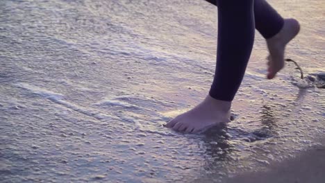 Frauenfüße,-Die-Zum-Sonnenuntergang-Im-Wasser-Am-Strand-Spazieren-Gehen