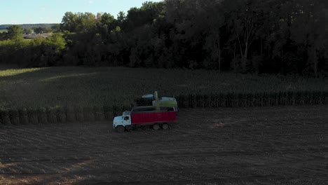 4K-aerial-view-panning-left-of-the-harvester-chopping-corn-into-a-truck-starting-in-the-shadows-at-golden-hour-moving-into-the-sun