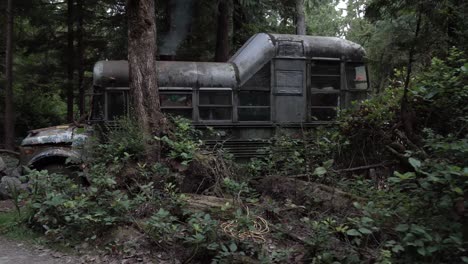 Man-comes-out-and-closes-door-of-rusty-bus-with-GMC-insignia-with-man-coming-out-of-it,-used-as-a-home-in-the-woods-of-Vancouver-Island,-Canada