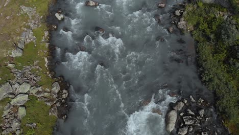 Glacial-meltwater-river-fast-flowing-downstream-in-summer,-Norway,-aerial-view