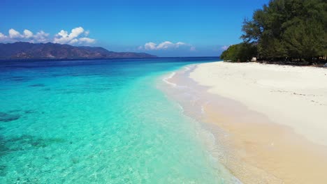 Island-In-Indonesia---Beautiful-Coral-Reef-Under-The-Crystal-Clear-Water,-Calm-Waves-Splashing-On-The-Sandy-Shore-Of-The-Lush-Island-With-Scenic-Mountain-In-The-Background---Closeup-Shot