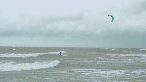 Surfistas-De-Kite-surf-Navegando-En-Las-Grandes-Olas-Del-Mar-Báltico-En-La-Playa-De-Liepaja-Karosta,-Día-De-Otoño-Nublado,-Tiro-Ancho-En-Cámara-Lenta