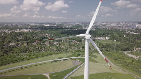 Drone-is-slowly-descending-alongside-a-wind-turbine,-Blue-sky,-white-Clouds-and-the-harbour-of-Hamburg-in-the-background
