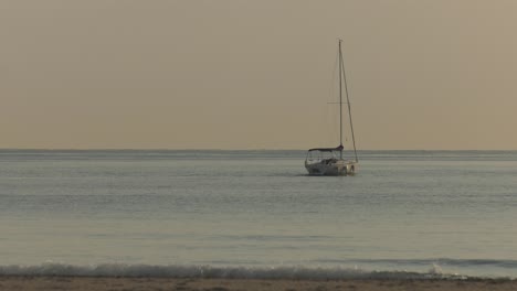 Calm-dawn-sea-with-sailing-yacht-heading-to-horizon,-sails-furled