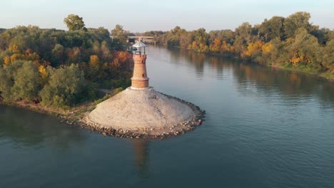 Aerial-drone-orbiting-around-the-old-stone-lighthouse-on-the-Danube-river-on-a-sunny-autumn-sunset-day