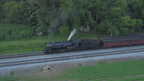Aerial-View-of-a-1924-Steam-Engine-with-Passenger-Train-Traveling-Along-the-Amish-Countryside-as-the-Sunsets-on-a-Summer-Day-as-Seen-by-a-Drone
