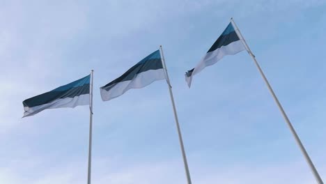 Tres-Banderas-De-Estonia-Ondeando-En-El-Viento-Contra-El-Cielo-Azul-En-Cámara-Lenta