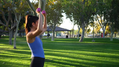 A-beautiful-and-fit-young-hispanic-woman-in-the-park-doing-a-dumbbell-shoulder-press-workout-exercise-SLOW-MOTION