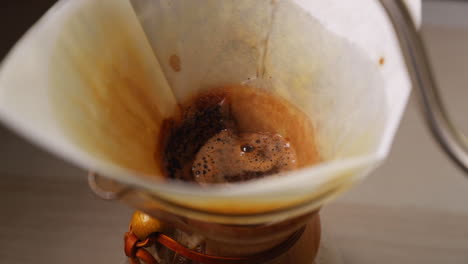 Gießen-Der-Kaffeekanne-Mit-Blick-Auf-Einen-Weißen-Filter-In-Einem-Glasgefäß-Zum-Auftropfen-Von-Kaffee,-Gießen-Von-Wasser-Auf-Einen-Kaffee-Und-Um-Den-Filter-Herum,-Gefangen-In-Zeitlupe-Mit-120-Fps