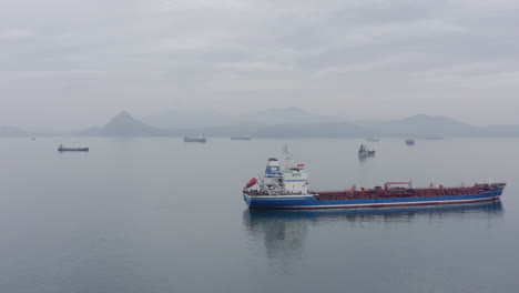 Ships-at-anchorage-waiting-area-in-a-calm-weather,-with-mountain-ridge-in-far-distance-on-the-overcast-day