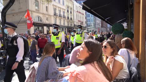 Menschen,-Die-Vor-Einem-Restaurant-Essen,-Beobachten-Demonstranten,-Die-Entlang-Der-Oxford-Street-Gegen-Sperren-Und-Impfpässe-Marschieren