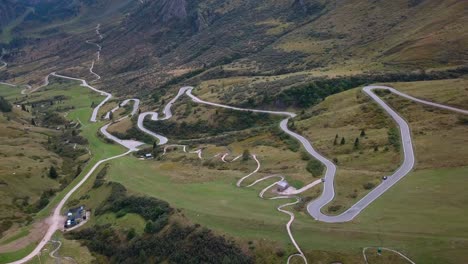 Long-winding-road-in-the-Dolomite-mountain-range-northern-Italy-with-cars-moving-near-the-meadow,-Aerial-drone-dolly-out-reveal-shot