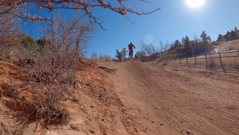 Guy-jumps-a-hill-on-a-dirt-track,-using-a-all-terrain-bike,-at-Red-Rocks-open-space-in-Colorado-Springs,-Colorado