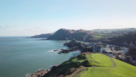 Overflying-The-Lush-Green-Capstone-Hill-On-A-Sunny-Day-With-A-View-Of-Harbour-And-Seaside-Town-Of-Ilfracombe,-North-Devon-Coast,-England,-United-Kingdom