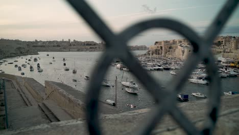 Camera-passes-behind-old-fence-showing-the-beautiful-harbour-of-Malta