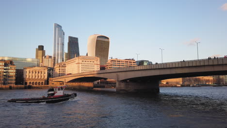 Freight-boat-passing-under-a-bridge-with-skyline-of-corporate-office-glass-buildings
