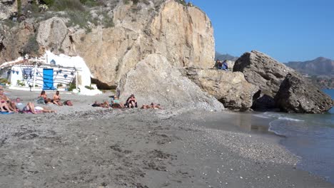 Tourists-Sunbathing-On-The-Sandy-Shore-Of-Calahonda-Beach-In-Nerja,-Malaga,-Spain-With-Sea-Waves-Splashing---panning-shot