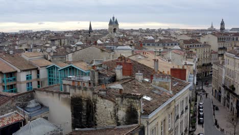 City-of-Bordeaux-France-rooftops-showing-Cailhau-City-Gate-and-pigeon-flocks-flying,-Aerial-pedestal-rise-reveal-shot