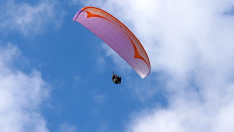 Paraglider-flying-against-cloudy-blue-sky,-low-angle-tracking-pan