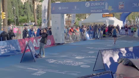 Marathonläufer-überquert-Die-Ziellinie,-Die-Uhr-Zeigt-Weniger-Als-Drei-Stunden-An,-Die-Kamera-Verfolgt-Das-Geschehen,-Malaga,-Spanien