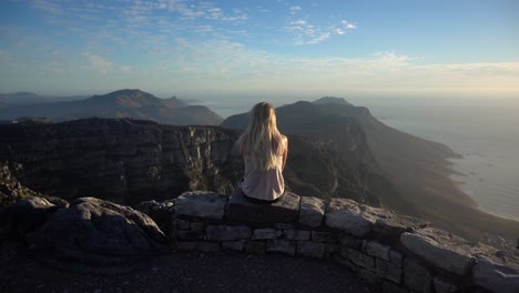 Slowmotion-Pulling-In-towards-a-Young-Blonde-Woman-Sitting-and-Looking-the-View-on-the-Table-Mountain-during-Sunset