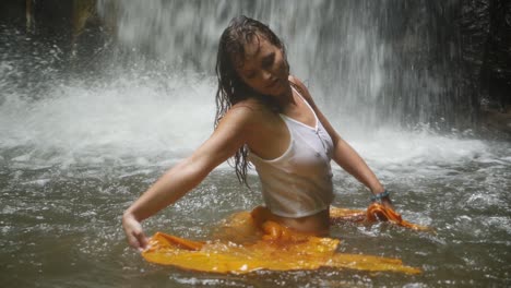 A-young-woman-with-long,-dark-hair-is-dancing-in-the-water-with-a-yellow-piece-of-fabric-in-slow-motion