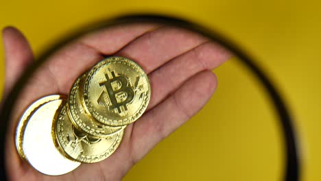 Close-up-of-person-looking-through-magnifier-of-hand-with-golden-bitcoins,investment
