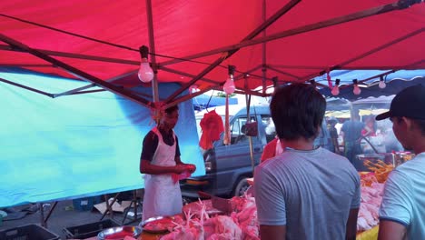 Young-man-selling-halal-poultry-at-outdoor-food-market-in-the-evening