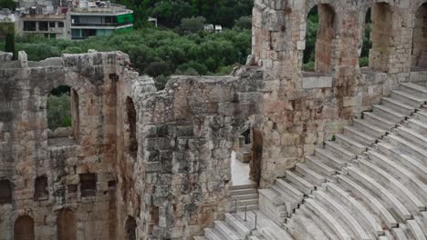 Aufsteigender-Blick-Auf-Die-Stufen-Und-Sitze-Des-Antiken-Römischen-Theaters-Odeon-Des-Herodes-Atticus-Auf-Dem-Filopappou-Hügel-In-Griechenland,-Mit-Bäumen-Und-Athenischen-Gebäuden-Im-Hintergrund