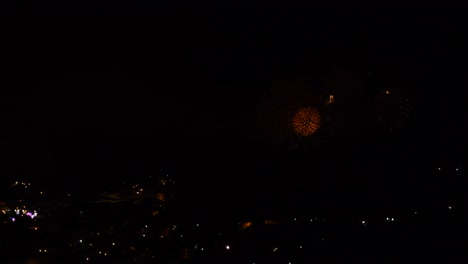 Celebration-with-many-golden-and-sparkling-fireworks,-over-a-mountain-town,-at-night