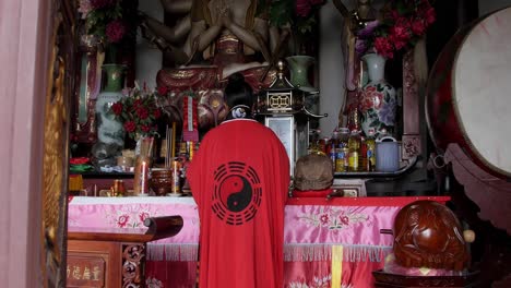 A-Taoist-female-monk-wearing-a-red-robe-with-the-yin-yang-symbol-at-the-altar-covered-with-pink-and-red-cloth---Wide-zoom-out