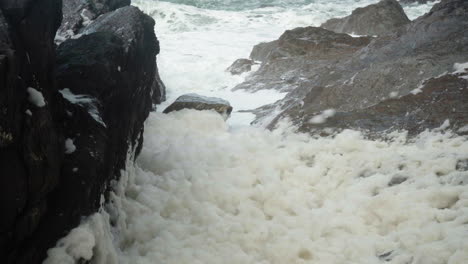 Ocean-Foam-Blown-By-The-Wind-And-Flying-By-The-Rocky-Beach-Of-Ilfracombe,-North-Devon-Coast,-England,-United-Kingdom