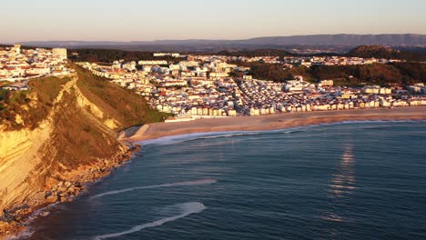 Town-of-Nazare-Portugal-during-sunset-golden-hour,-Aerial-pan-right-reveal