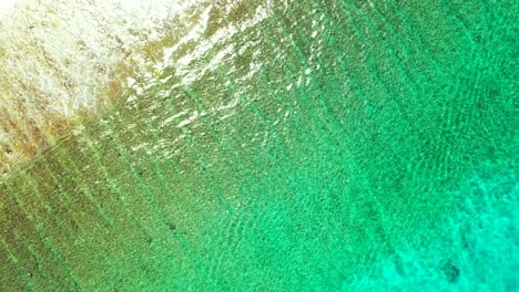 Beautiful-colorful-sea-texture-with-clean-water-of-turquoise-lagoon-over-sandy-seabed-reflecting-sunlight-and-white-waves-in-Bahamas