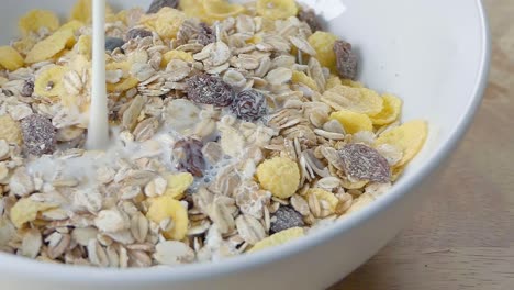 Slow-Motion-Slider-Shot-of-Pouring-Milk-onto-Muesli-in-a-White-Cereal-Bowl-on-a-Kitchen-Counter-for-Breakfast