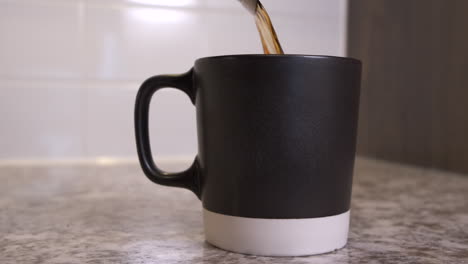 Freshly-brewed-filter-coffee-being-poured-from-metal-carafe-into-mug-in-slow-motion