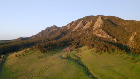 Beautiful-early-morning-sunrise-shining-warm-light-on-Colorado-Flatiron-mountains,-trees,-and-Chautauqua-trail-for-hiking-near-Boulder-with-aerial-drone-flight
