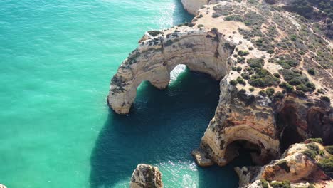 Ocean-eroded-rock-arch-formations-in-Marinha-Beach-south-of-Portugal,-Aerial-approach-shot